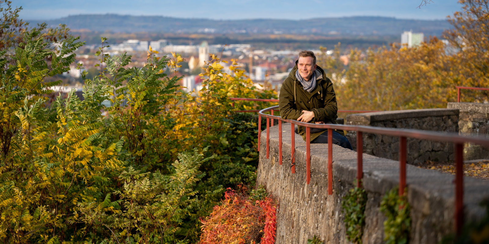 Benedikt Doll sitzt auf einer Brücke. Im Hintergrund die Stadt.
