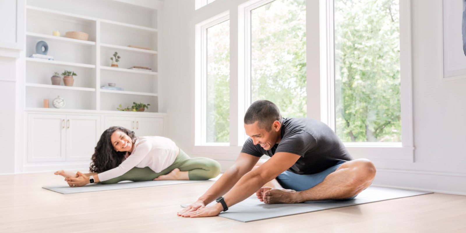 Mann und Frau machen Dehnübungen zuhause auf Yogamatte