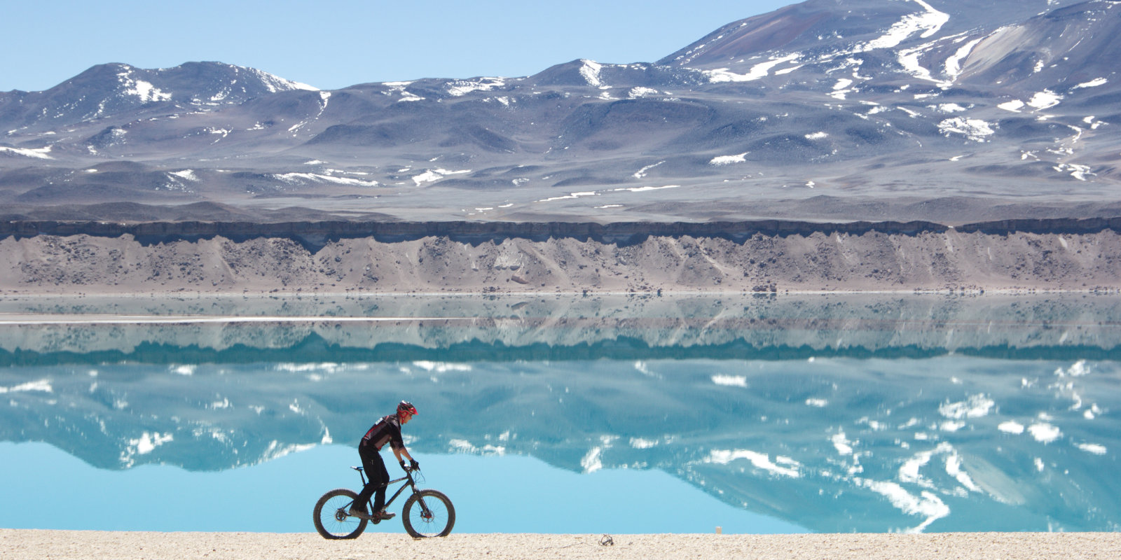 Guido Kunze fährt mit dem Rad an einem Stausee. Im Hintergrund Berge