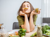 Junge Frau sitzt mit vielem grünen Gemüse am Tisch