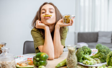 Junge Frau sitzt mit vielem grünen Gemüse am Tisch