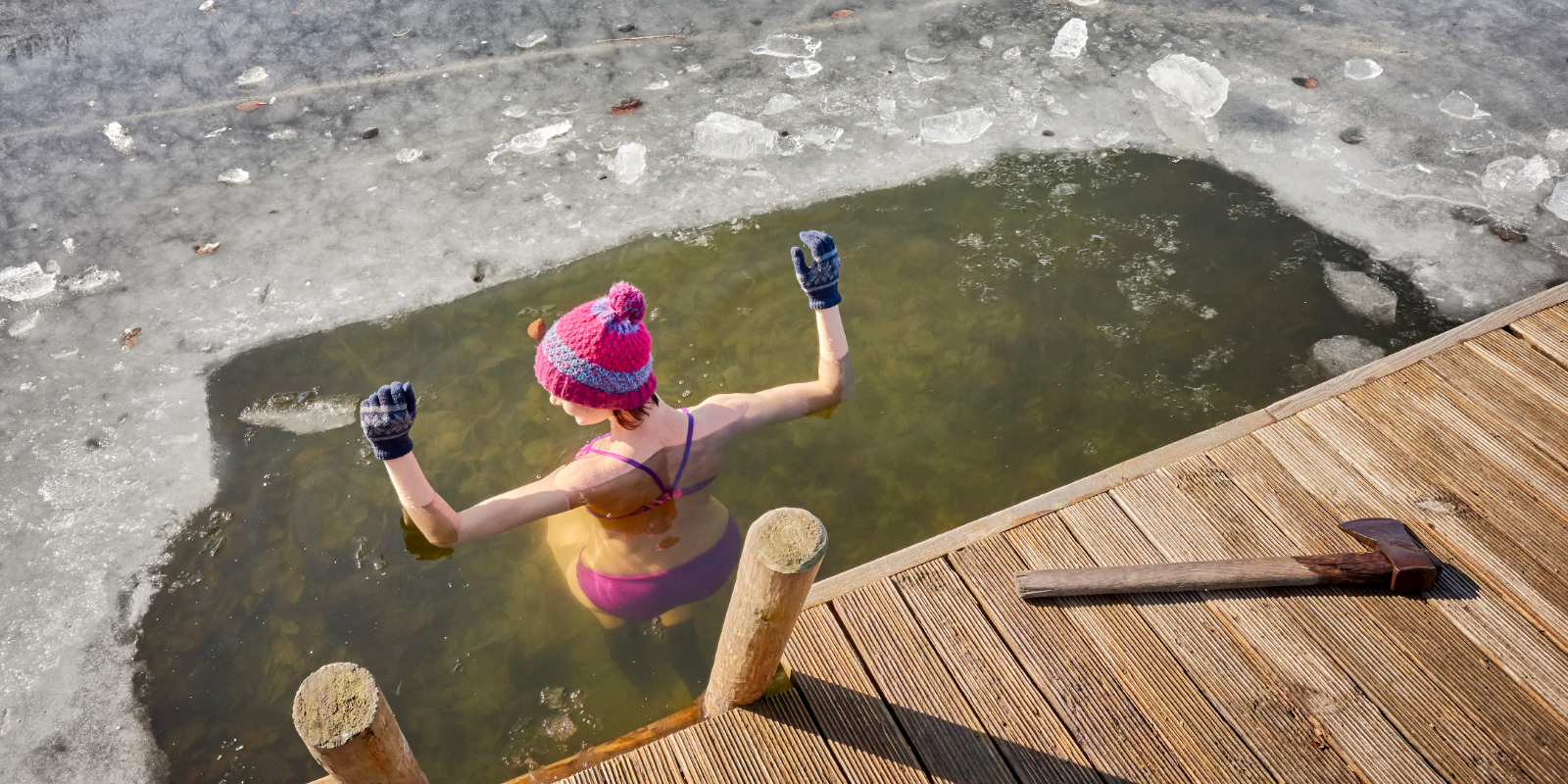 Frau badet im Winter in einem See mit Mütze und Handschuhen