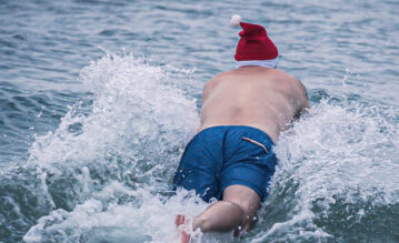 Mann springt im Winter mit Weihnachtsmütze ins eiskalte Meer