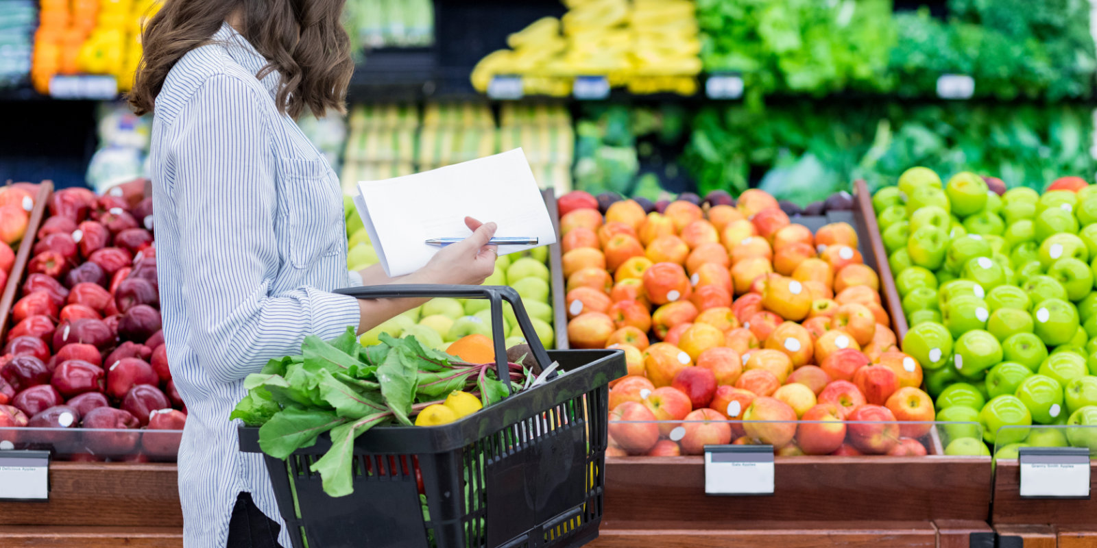 Frau mit Einkaufsliste im Supermarkt am Gemüseregal