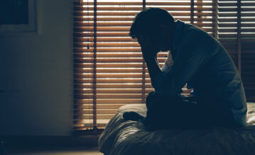 Mann mit Fatigue sitzt erschöpft auf dem Bett