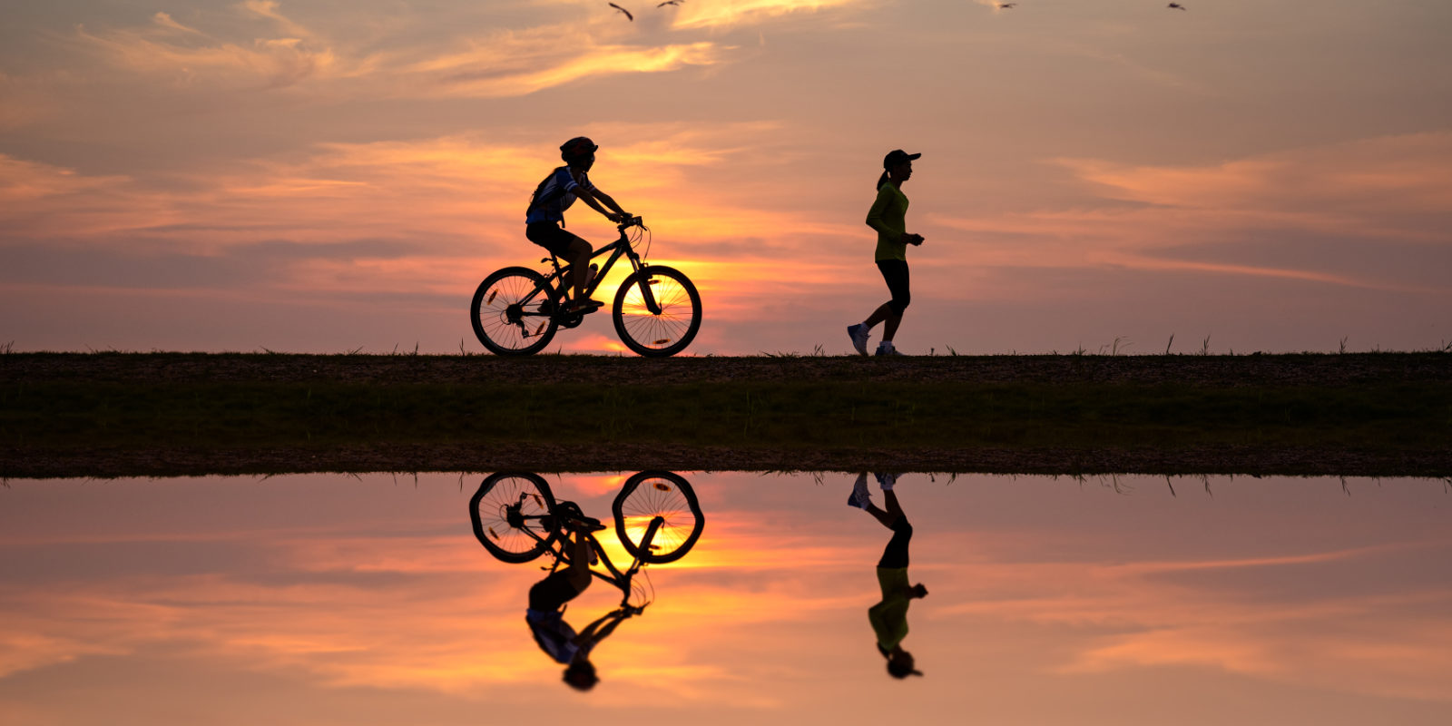 Radfahrer und Läuferin laufen an einem See entlang