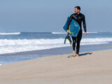 Mann geht mit seinem Bodyboard und Flossen am Strand entlang und guckt auf das Meer