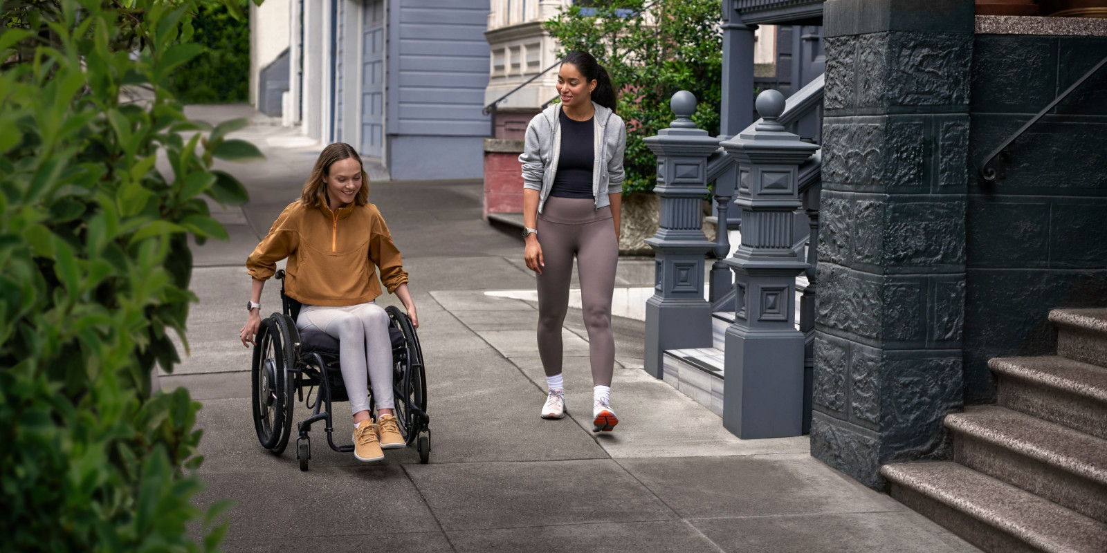 Rollstuhlfahrerin mit Garmin Venu 3 am Handgelenk fährt mit ihrer Freundin spazieren