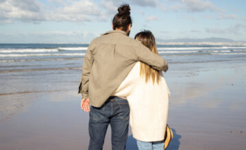Paar mit einem Größenunterschied steht vor dem Meer und umarmt sich