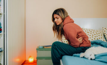 Frau sitzt mit Periodenschmerzen auf ihrem Bett und krümmt sich