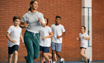Kinder und Lehererin laufen beim Schulsport im Kreis