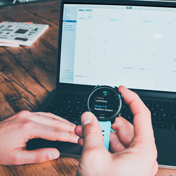 Redakteur Olli hält seine Garmin Uhr in der Hand, auf der sein Lauftraining im Kalender zu sehen ist. Im Hintergrund ist ein geöffneter Laptop mit seinem Kalender zu sehen