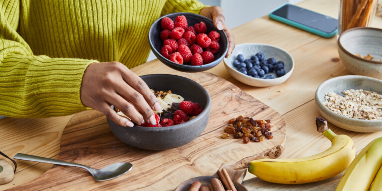 Frau bereitet sich ein Frühstück nach der Mind-Diät zu und füllt Beeren, Bananen und Haferflocken in eine Müslischale