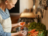 Junge blonde Frau kocht eine Suppe und gibt geschnittene Karotten in einen Topf