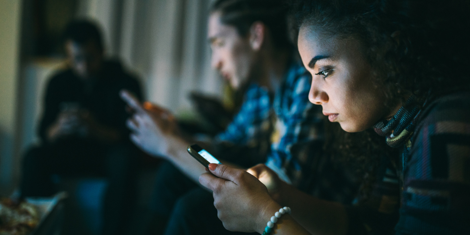 Junge Frau sitzt mit Freunden auf der Couch und alle starren auf ihr Smartphone