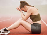 Frau mit dem Post Race Blues sitzt deprimiert und traurig auf der Tartanbahn