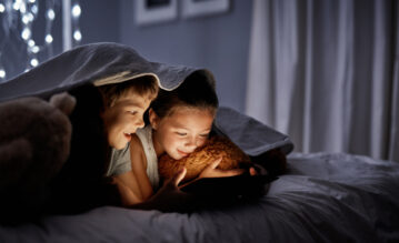 Junge und Mädchen liegen im Bett und spielen mit dem Handy