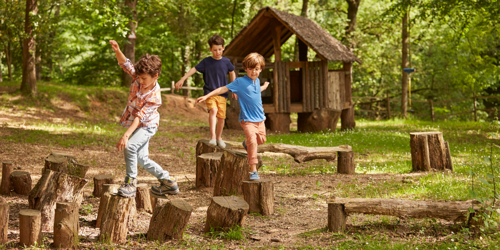 Drei Kinder spielen zusammen auf einem Spielplatz und klettern über Baumstümpfe