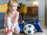 Kleines, blondes Mädchen schnürt ihre Sportschuhe