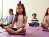 Kinder sitzen auf ihren Yogamatten und meditieren zu Beginn der Yogastunde