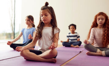 Kinder sitzen auf ihren Yogamatten und meditieren zu Beginn der Yogastunde