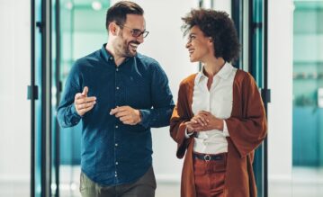 Zwei Personen gehen bei einem Walk and Talk Meeting durch einen Büroflur und unterhalten sich.