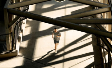 Junger Mann läuft beim Training in der Stadt über eine Brücke. Am Handgelenk trägt er einen Forerunner 970 von Garmin.