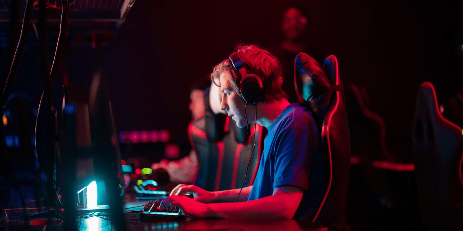 Eine Person spielt mit Headset an einem PC in einem mit farblichen Lampen ausgeleuchteten Raum.