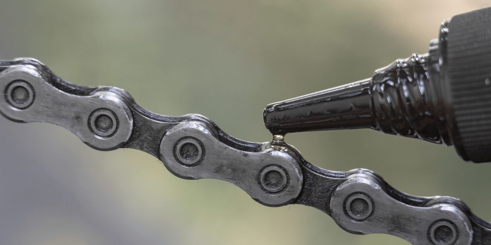 Aus einer kleinen Flasche fließt Öl auf eine Fahrradkette.
