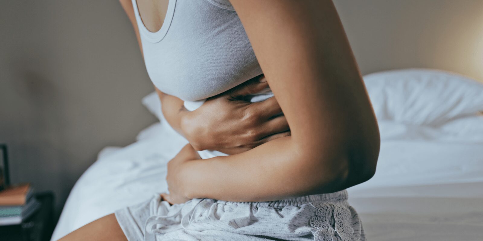 Frau sitzt im Bett und hält sich den Bauch