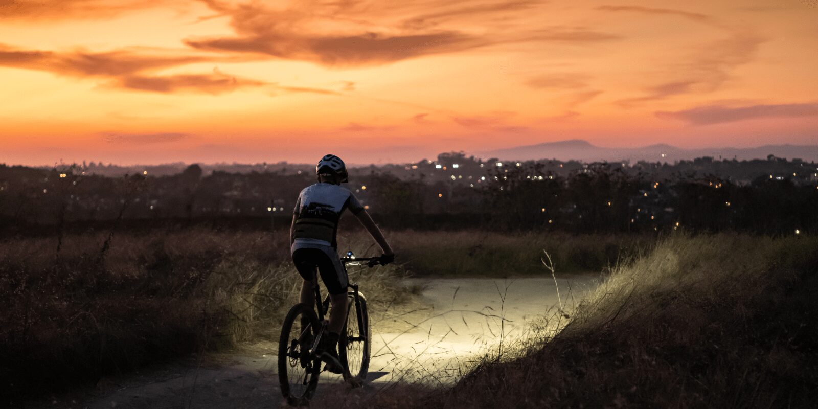Eine Radfahrerin fährt während des Sonnenuntergangs über einen leeren Feldweg.