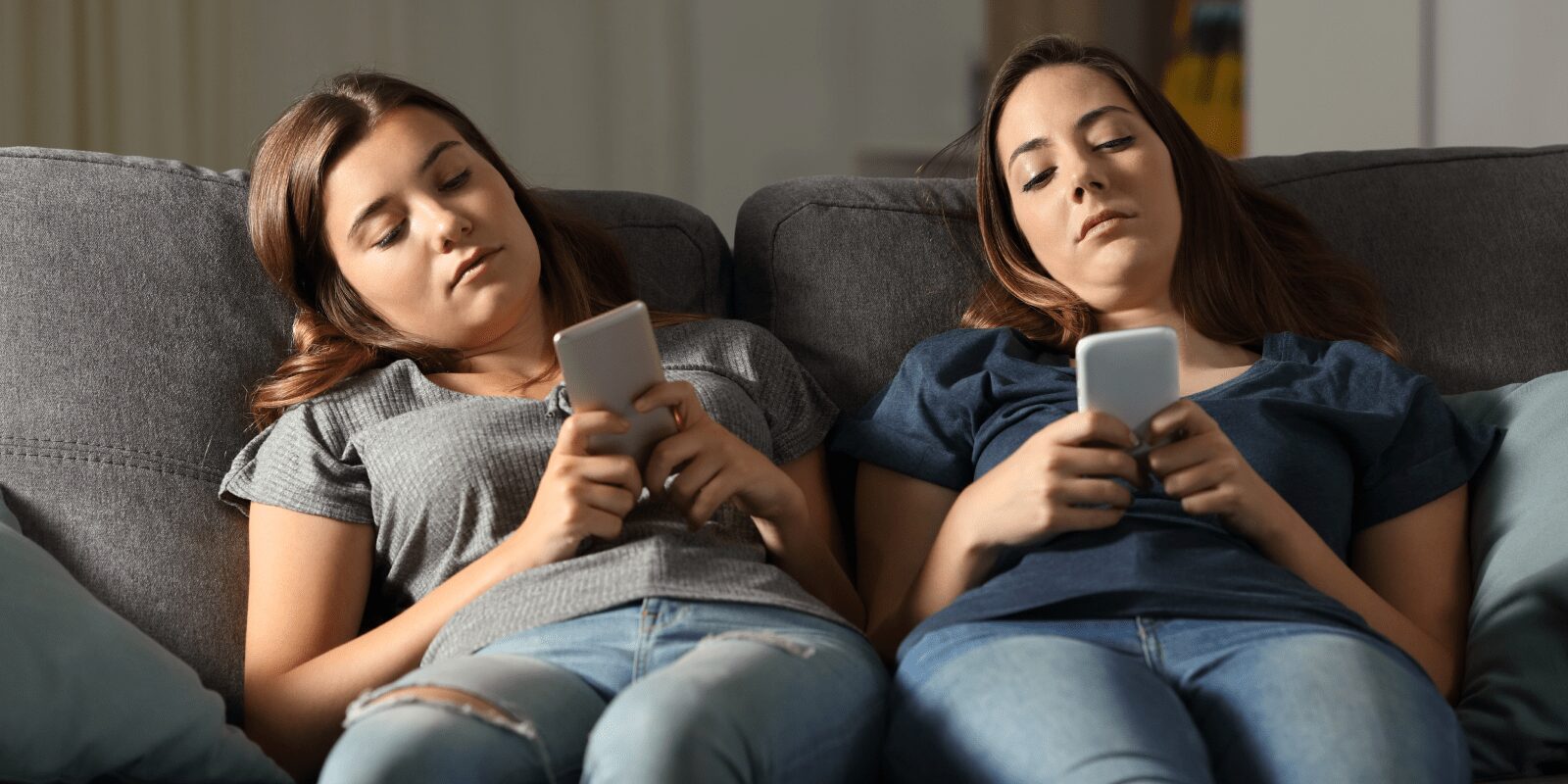 Zwei Frauen sitzen auf der Couch und schauen gelangweilt auf ihre Handys.