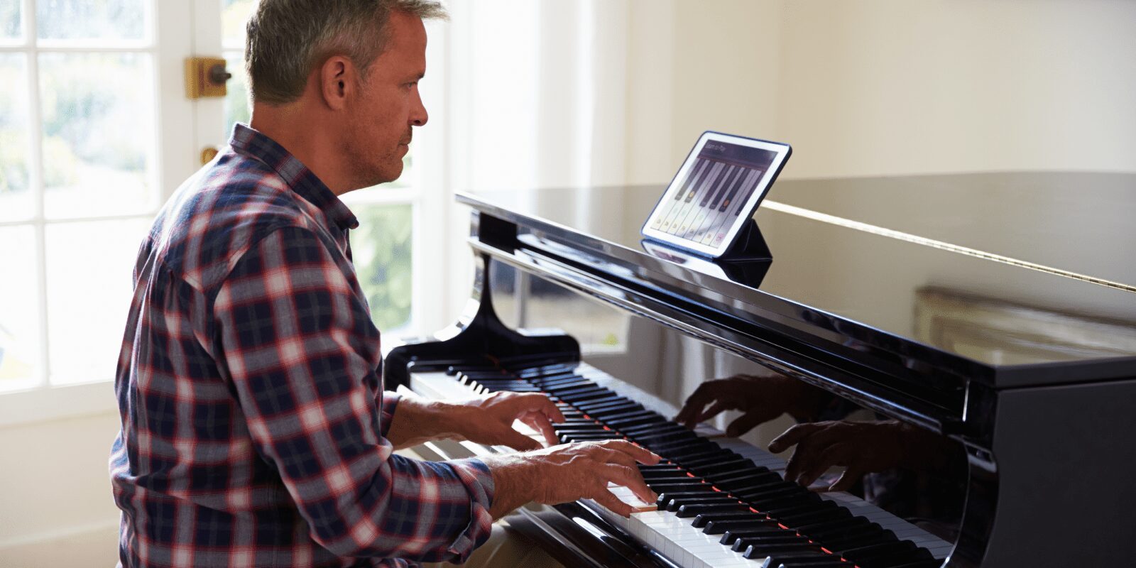 Ein Mann sitzt am Klavier und lernt mit einem Tablet ein Stück.