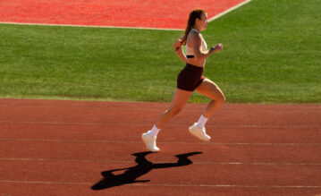 Junge Frau mit Garmin Forerunner 970 am Handgelenk läuft über eine Tartanbahn