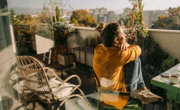 Eine Frau sitzt auf ihrem Balkon in der Sonne und schaut in die Ferne.